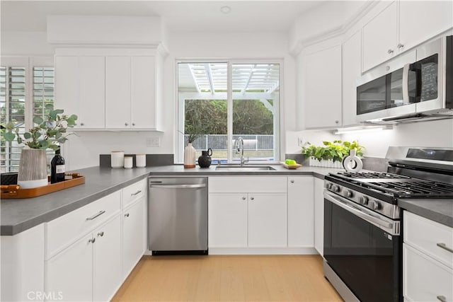 kitchen featuring a sink, dark countertops, appliances with stainless steel finishes, white cabinets, and light wood finished floors