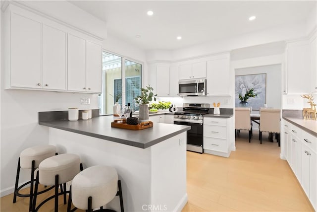 kitchen with a breakfast bar area, recessed lighting, stainless steel appliances, white cabinets, and dark countertops