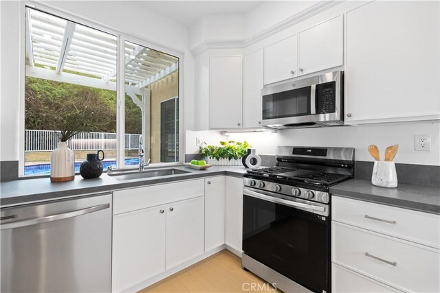 kitchen featuring dark countertops, light wood-type flooring, appliances with stainless steel finishes, white cabinets, and a sink