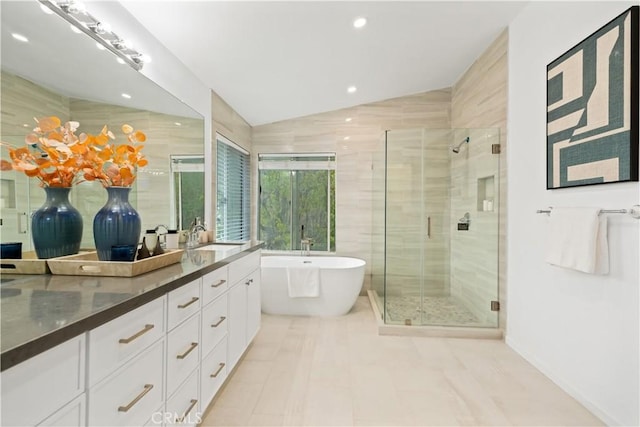 full bathroom featuring vanity, lofted ceiling, a stall shower, a freestanding bath, and tile walls