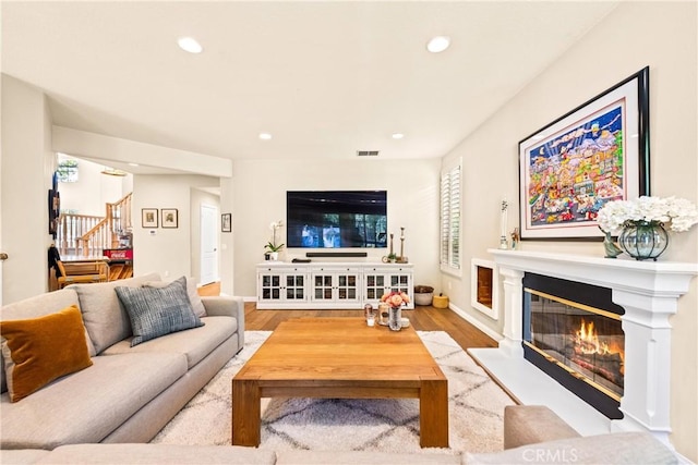 living area with wood finished floors, a glass covered fireplace, recessed lighting, baseboards, and stairs