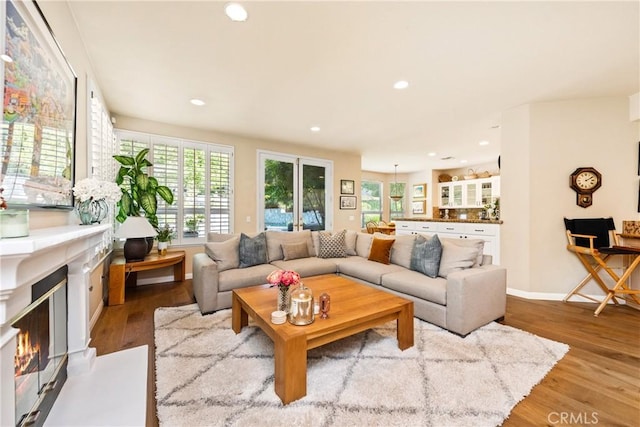 living room featuring a glass covered fireplace, recessed lighting, baseboards, and wood finished floors