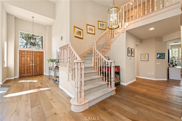 foyer entrance featuring baseboards, a chandelier, a towering ceiling, and hardwood / wood-style flooring