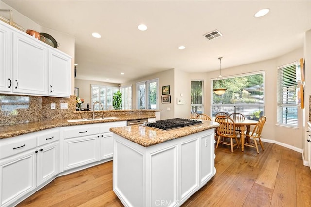 kitchen with tasteful backsplash, a wealth of natural light, light wood-style floors, white cabinetry, and a sink