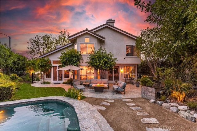 back of house at dusk featuring fence, stucco siding, a chimney, a fire pit, and a patio area