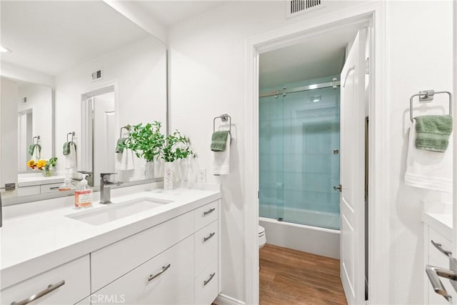 bathroom featuring visible vents, toilet, wood finished floors, shower / bath combination with glass door, and vanity