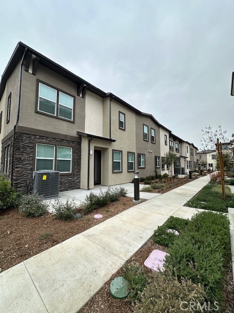 townhome / multi-family property with stucco siding, stone siding, a residential view, and cooling unit