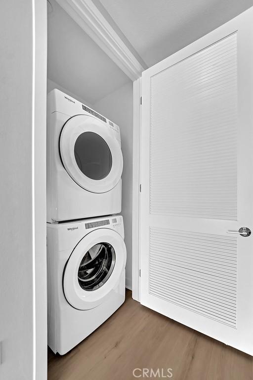 laundry room featuring stacked washer / drying machine, wood finished floors, and laundry area