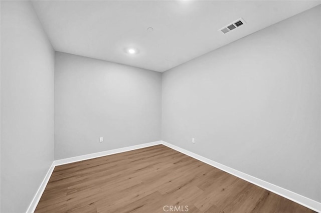 empty room with wood finished floors, visible vents, and baseboards