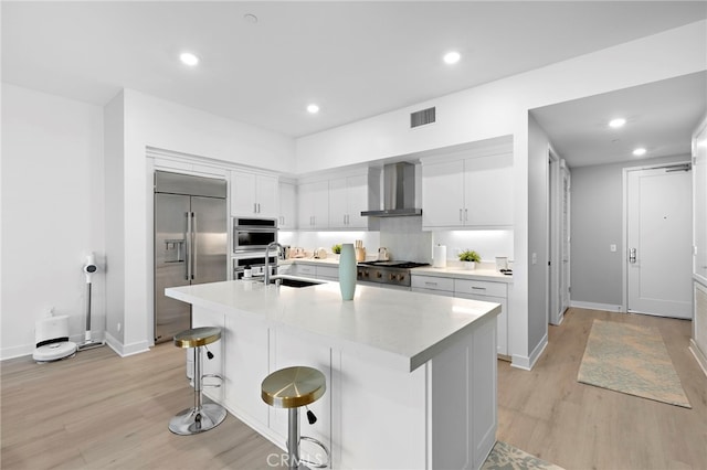 kitchen with visible vents, a sink, appliances with stainless steel finishes, wall chimney exhaust hood, and light countertops