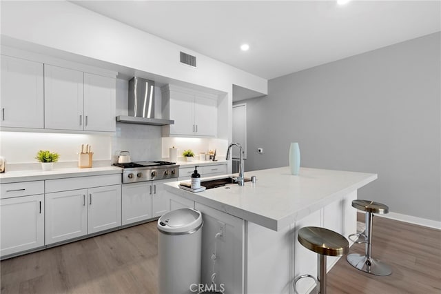 kitchen featuring visible vents, a breakfast bar, a sink, wall chimney range hood, and stainless steel gas cooktop