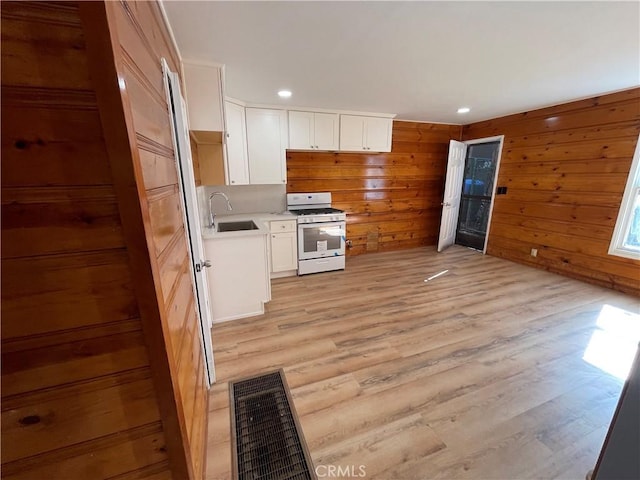 kitchen with light wood-type flooring, a sink, white gas range oven, white cabinetry, and light countertops