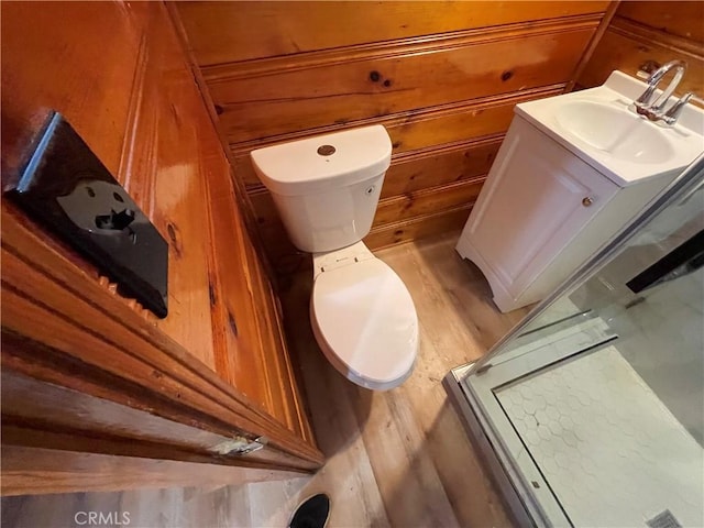 bathroom featuring wooden walls, toilet, a shower with shower door, wood finished floors, and vanity