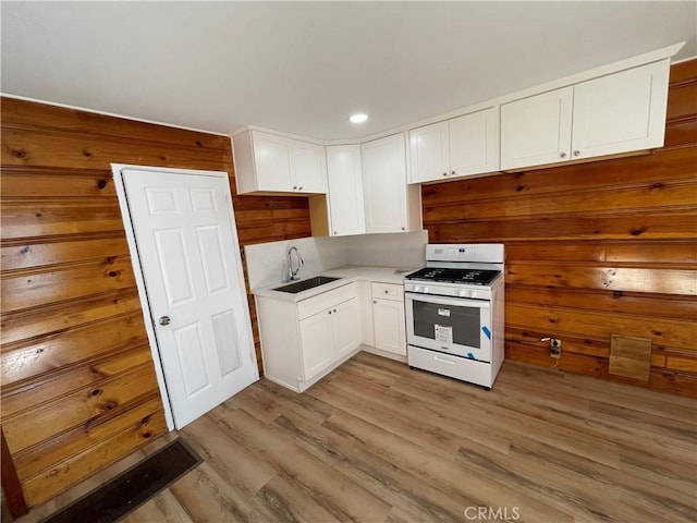 kitchen with a sink, light wood-style floors, white gas range, and white cabinetry