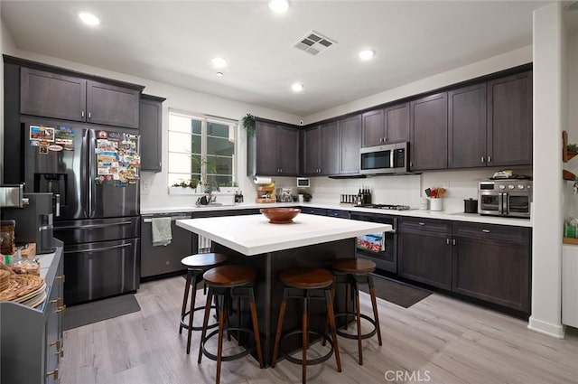 kitchen with dark brown cabinets, visible vents, a kitchen breakfast bar, and appliances with stainless steel finishes