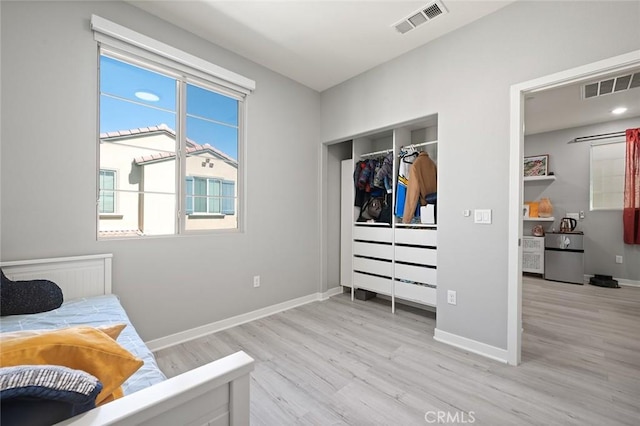 bedroom featuring light wood-type flooring, visible vents, baseboards, and a closet