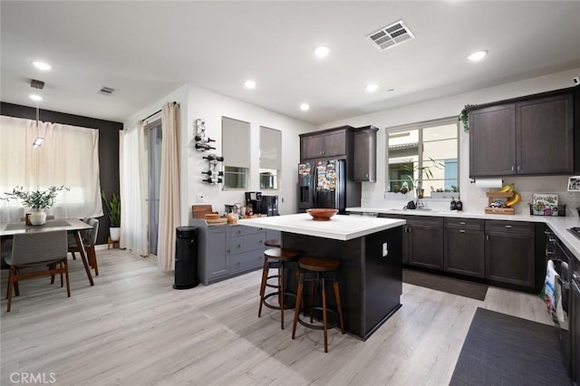 kitchen featuring visible vents, a kitchen bar, black fridge, a center island, and light countertops