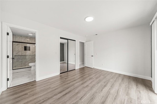 unfurnished bedroom with ensuite bath, wood finished floors, and baseboards