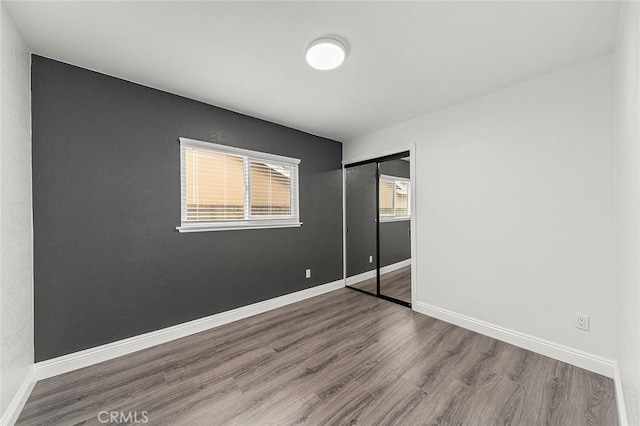 unfurnished bedroom featuring a closet, baseboards, and wood finished floors