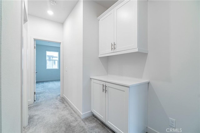 hallway featuring baseboards and light colored carpet