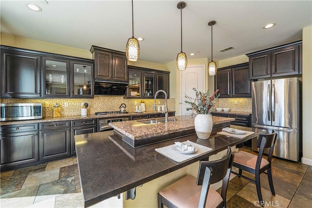 kitchen with a breakfast bar area, an island with sink, a sink, stainless steel appliances, and tasteful backsplash