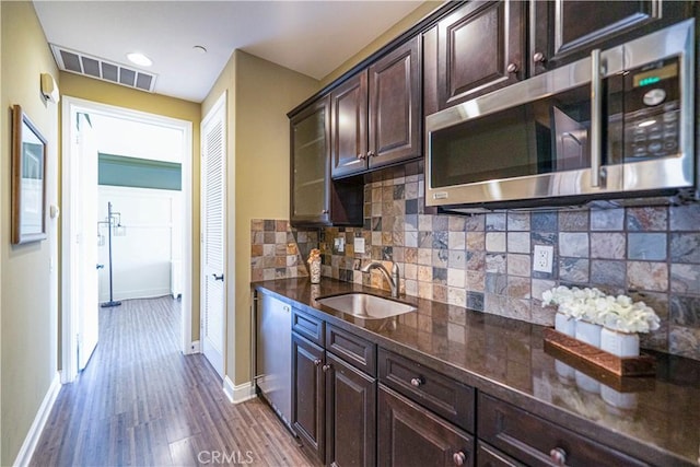 kitchen featuring stainless steel microwave, dark brown cabinets, visible vents, dark wood-type flooring, and a sink