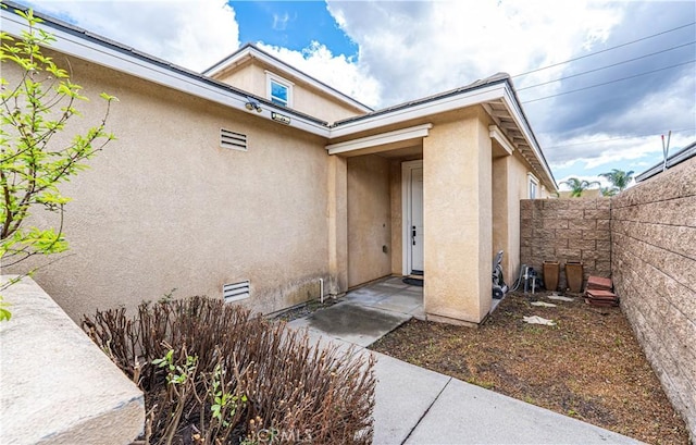 entrance to property featuring fence and stucco siding