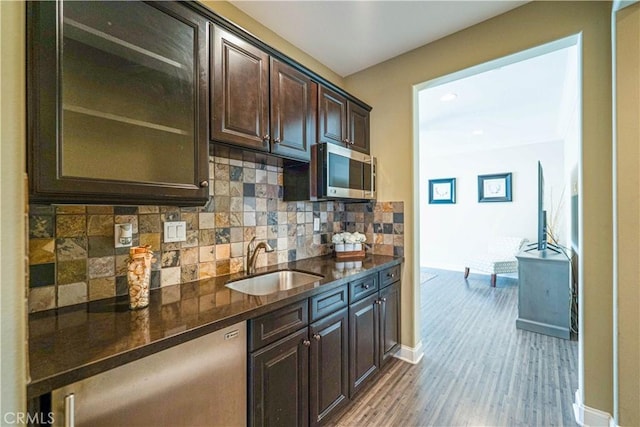 kitchen featuring light wood-type flooring, a sink, stainless steel microwave, tasteful backsplash, and dark brown cabinets