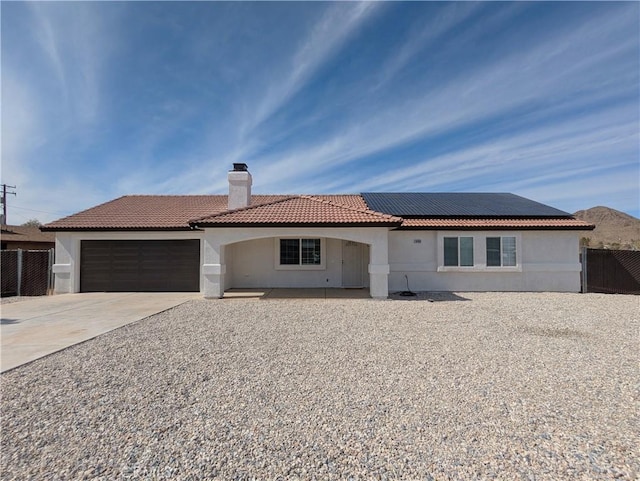 view of front of property featuring stucco siding, roof mounted solar panels, fence, a garage, and a chimney