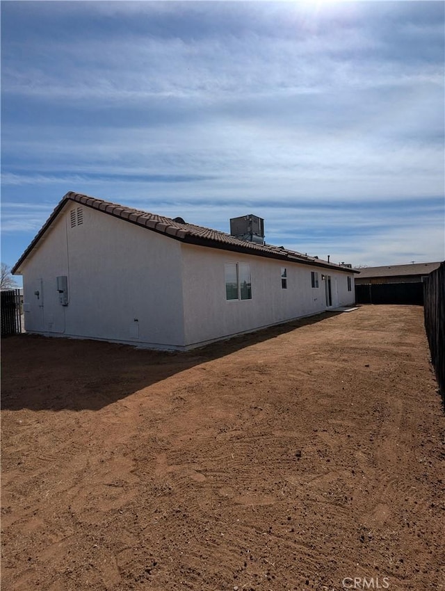 view of side of property featuring a tile roof, central air condition unit, fence, and stucco siding