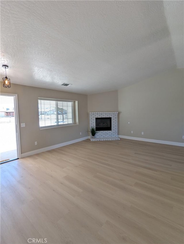 unfurnished living room featuring a brick fireplace, light wood-style floors, visible vents, and baseboards