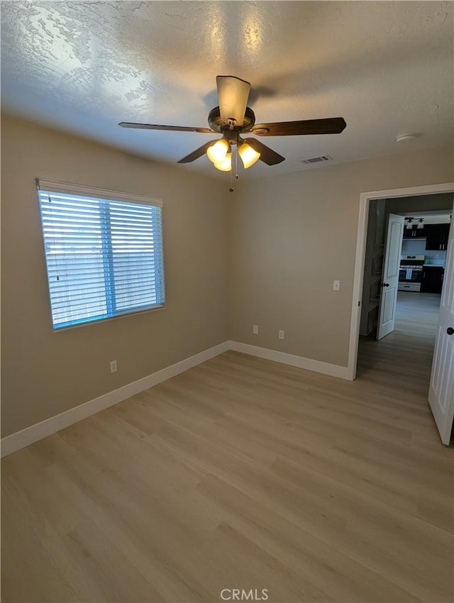 spare room with light wood-style flooring, visible vents, baseboards, and a textured ceiling