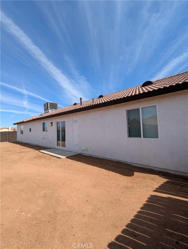 rear view of property featuring fence, central air condition unit, a tile roof, stucco siding, and a patio