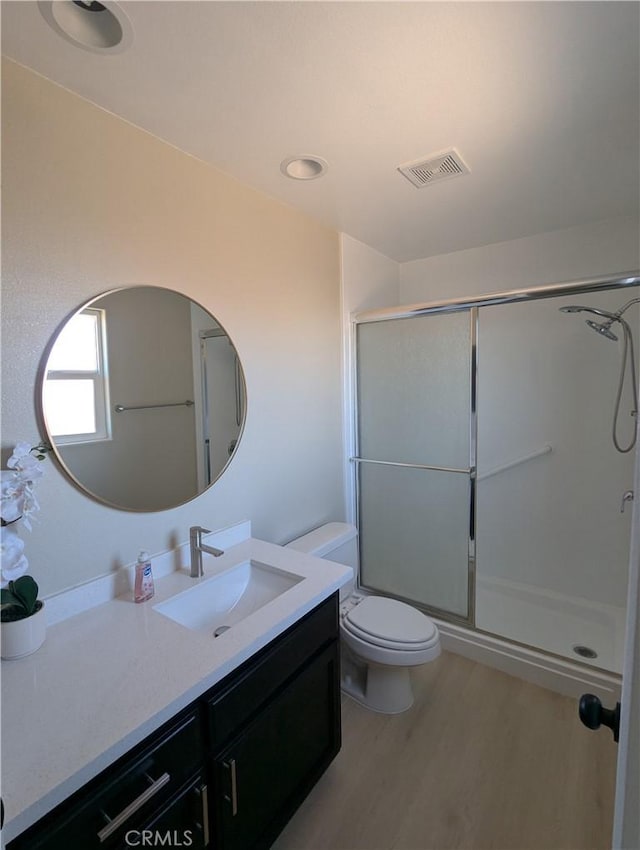 bathroom with a shower with shower door, visible vents, toilet, wood finished floors, and vanity