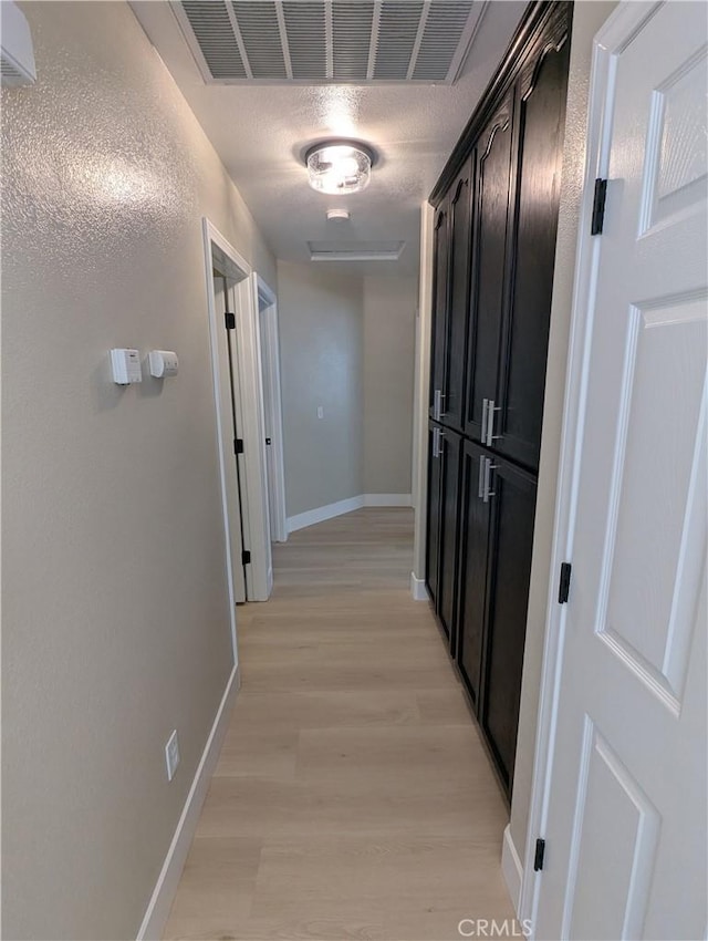 hallway with light wood-style floors, visible vents, and baseboards