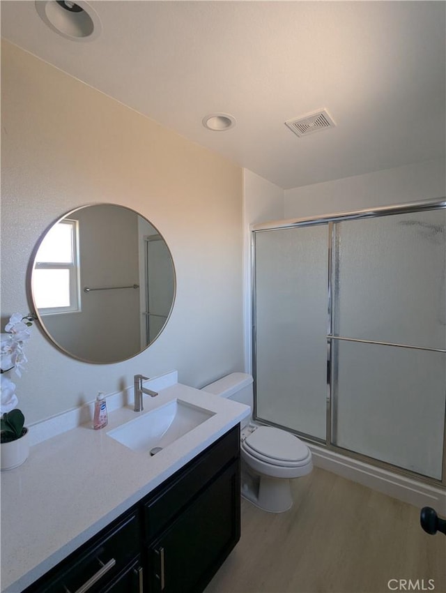 full bathroom featuring a shower with shower door, visible vents, toilet, and wood finished floors