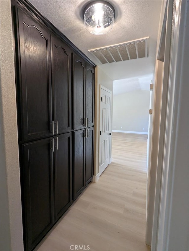 hallway with visible vents, baseboards, a textured ceiling, and light wood-style flooring