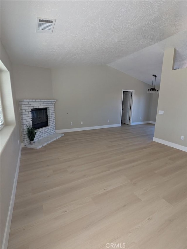 unfurnished living room with light wood finished floors, visible vents, a brick fireplace, vaulted ceiling, and a textured ceiling