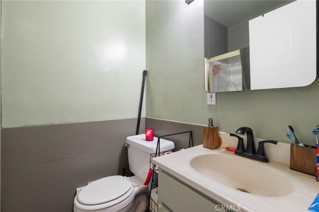 bathroom featuring vanity, tile walls, toilet, and a wainscoted wall