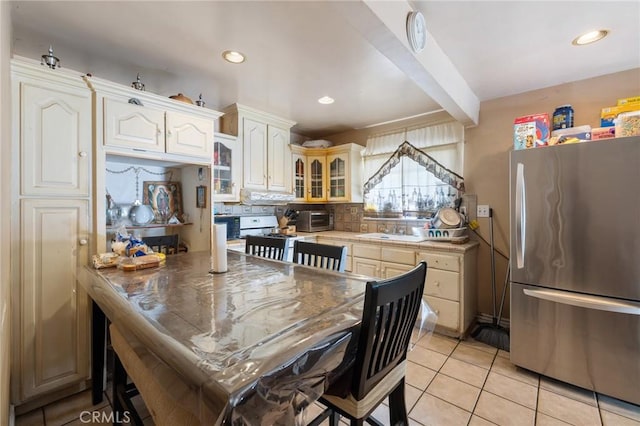 kitchen with light tile patterned flooring, recessed lighting, freestanding refrigerator, glass insert cabinets, and backsplash