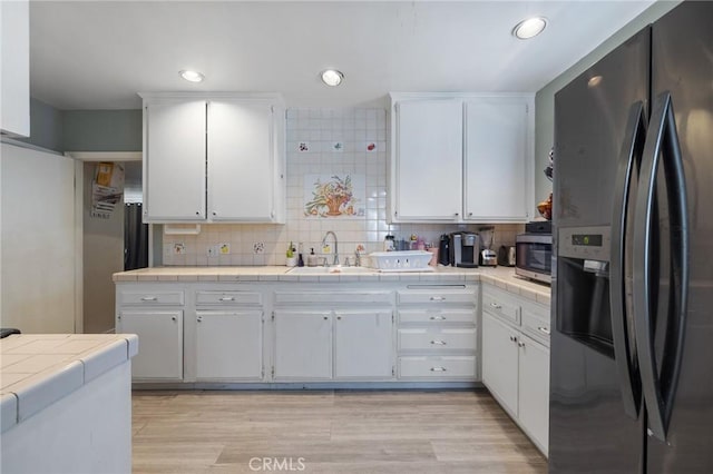 kitchen featuring a sink, decorative backsplash, tile counters, stainless steel microwave, and black fridge