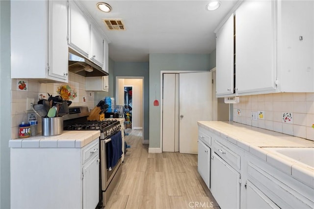 kitchen featuring tile countertops, visible vents, under cabinet range hood, white cabinetry, and gas range