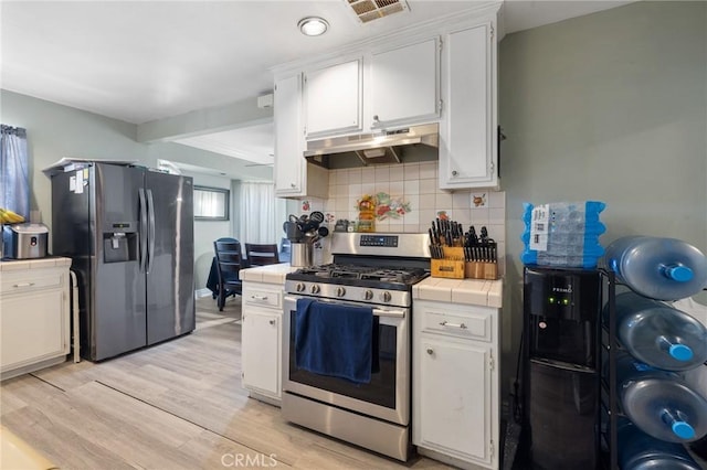 kitchen featuring light wood finished floors, visible vents, tile counters, under cabinet range hood, and stainless steel appliances