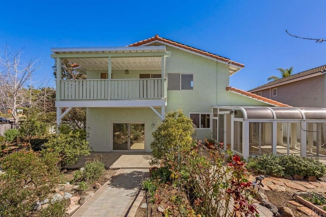 rear view of house featuring stucco siding, a tile roof, a patio, a sunroom, and a balcony