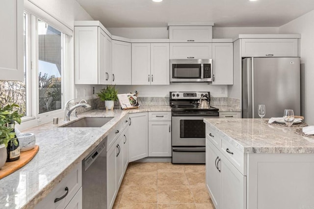 kitchen featuring a sink, light stone counters, appliances with stainless steel finishes, and white cabinets