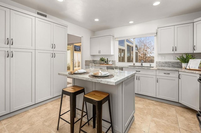 kitchen featuring light stone countertops, a breakfast bar, recessed lighting, a sink, and a center island