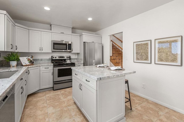 kitchen featuring a kitchen island, baseboards, light stone countertops, appliances with stainless steel finishes, and a kitchen breakfast bar