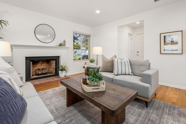 living area featuring recessed lighting, a fireplace with raised hearth, baseboards, and wood finished floors