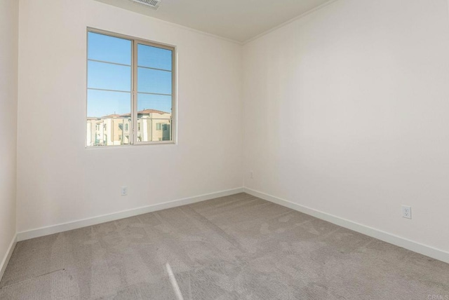 empty room featuring crown molding, light colored carpet, baseboards, and visible vents