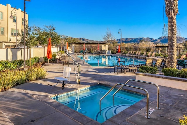 view of swimming pool featuring a patio, a community hot tub, fence, and a mountain view